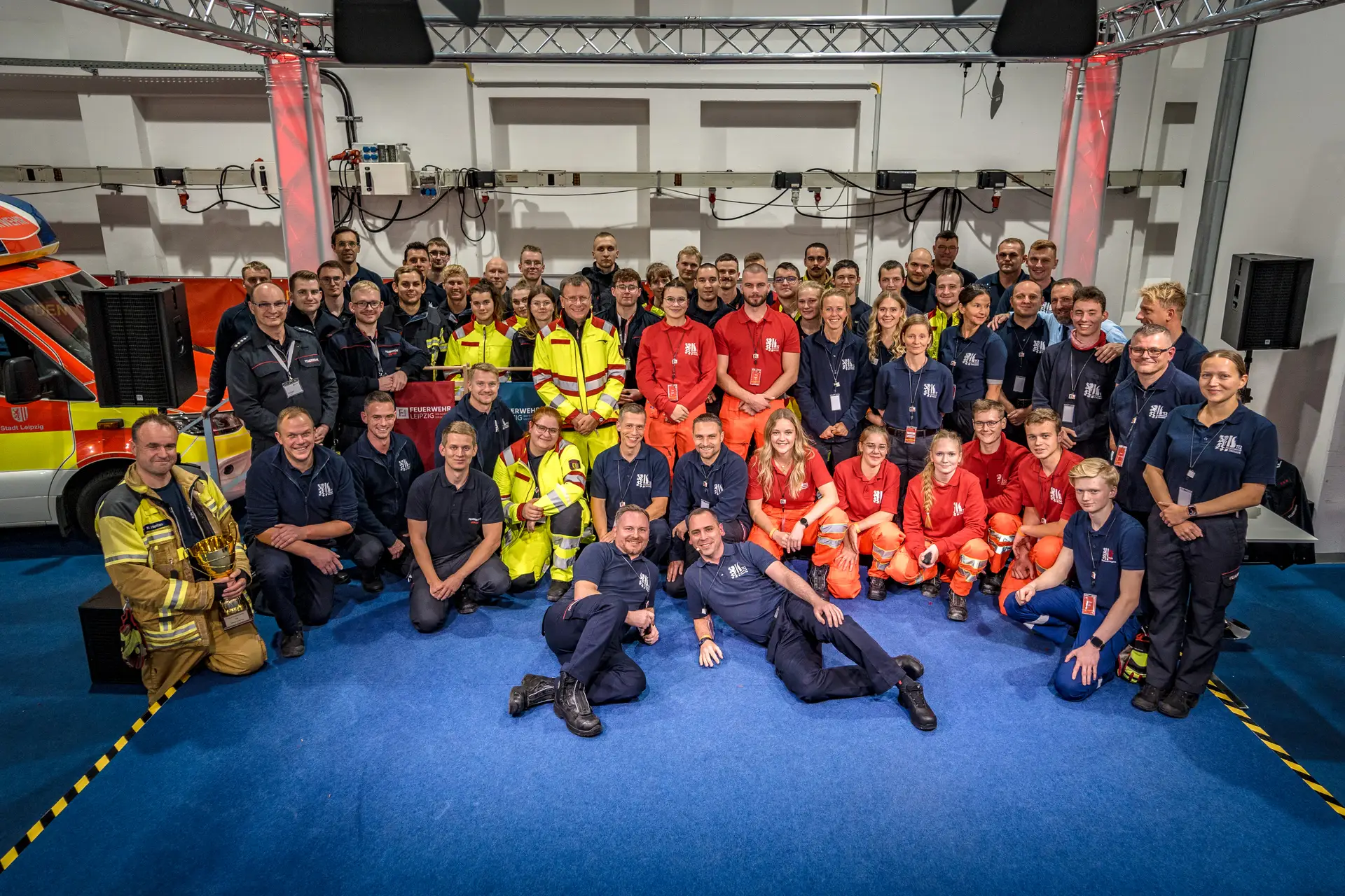 Gruppenfoto des Messeteams der Feuerwehr Dresden in einer Halle; einige Personen tragen Rettungsdienstkleidung, links steht ein Einsatzfahrzeug.